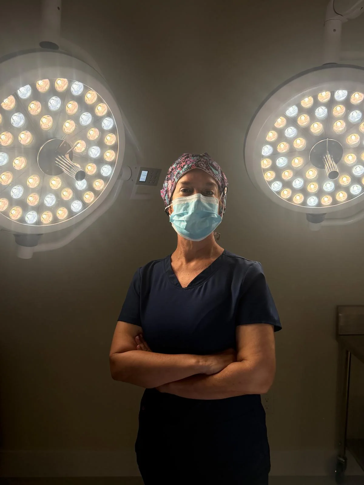 Dr. Kyrenia Sanchez Rodriguez wearing surgical scrubs and a mask beneath examination lights